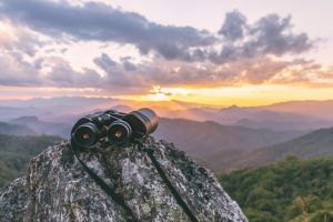 Binoculars on top of rock mountain at sunset. Analogy with web design and overlooking certain key elements in website optimization.